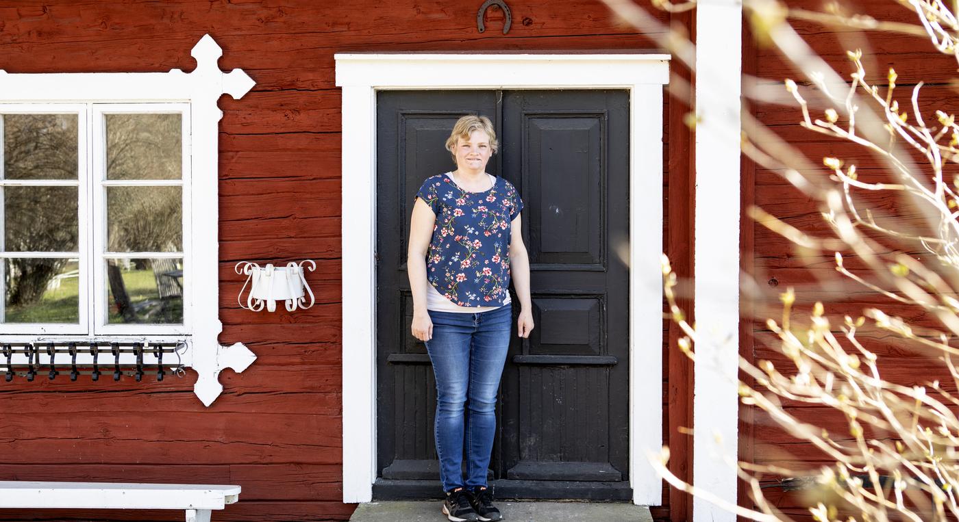 En kvinna på trappan till ett gammalt hus falu rödfärg med vita dörr- och fönsterkarmar.