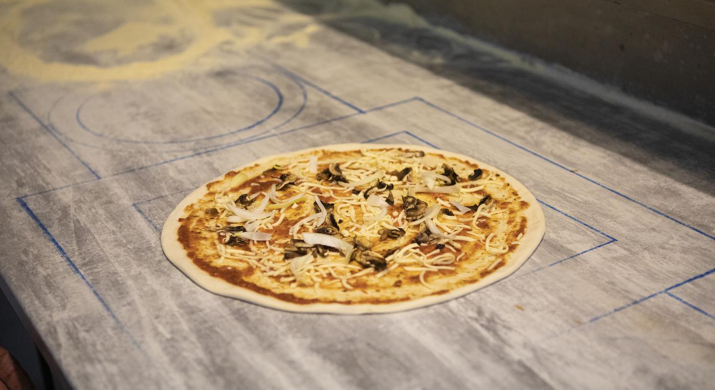 Pizza med ost och champinjoner på bakbord i trä.