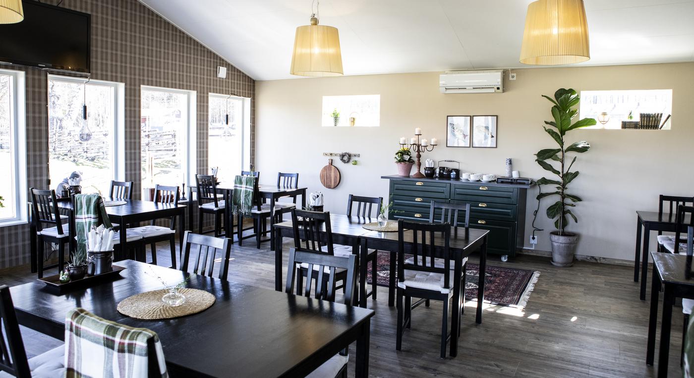 En restauranglokal med svarta bord och stolar, ljusa väggar och stora fönster.