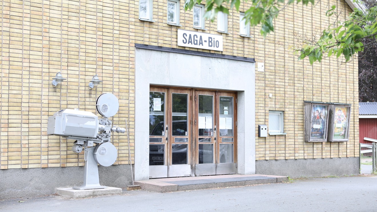 En gul tegelbyggnad med skylten Saga-bio. Utanför står en gammal projektor.