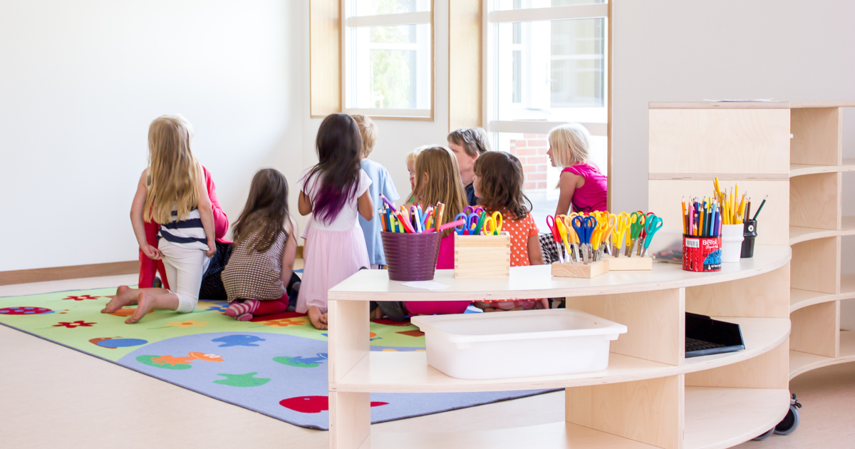 Barn sitter tillsammans i en förskolemiljö med lekmatta och pysselmaterial.