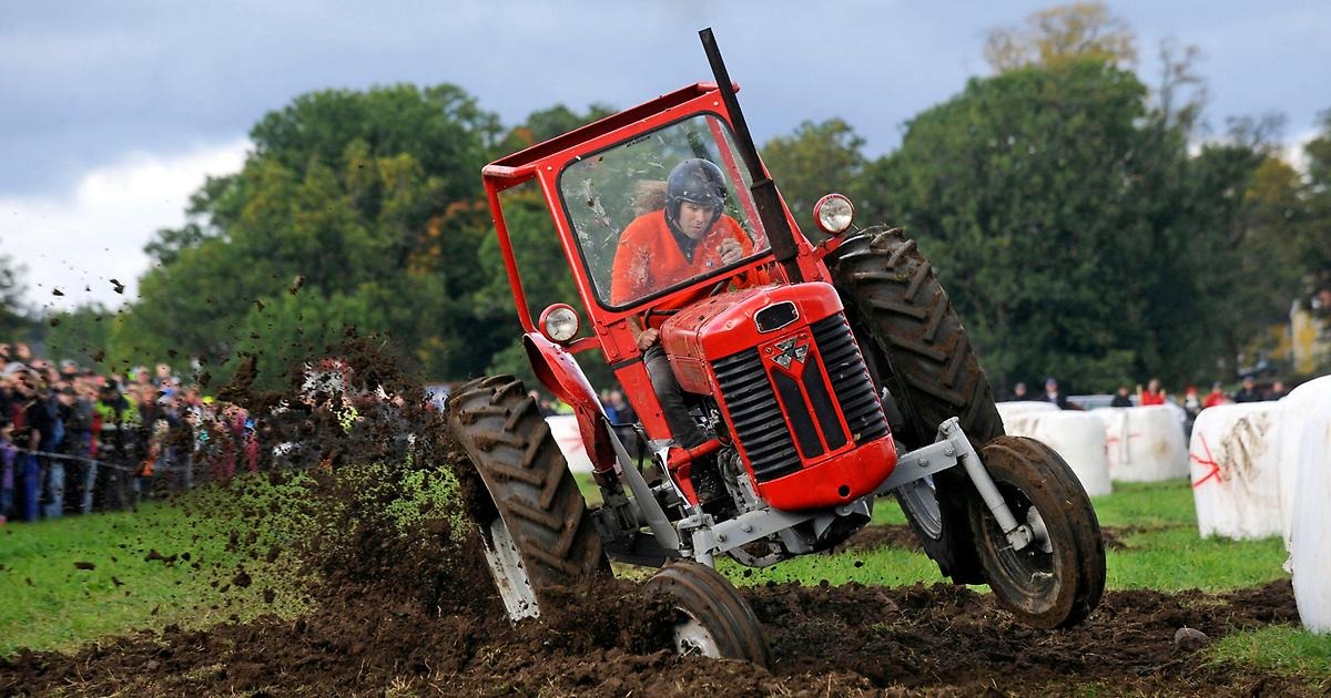 En blå traktor av märket Ford susar fram. Bakom ratten sitter en ung man med integralhjälm.m.