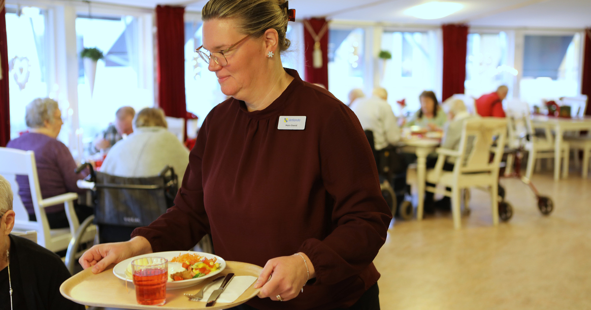Kvinna står i en matsal och håller i en bricka med mat 