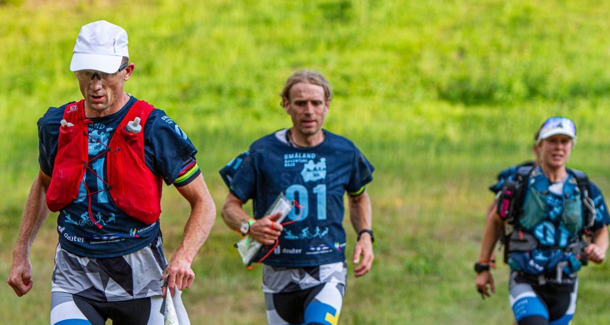 Tre tävlingsdeltagare tar sig fram med karta och kompass i hand.