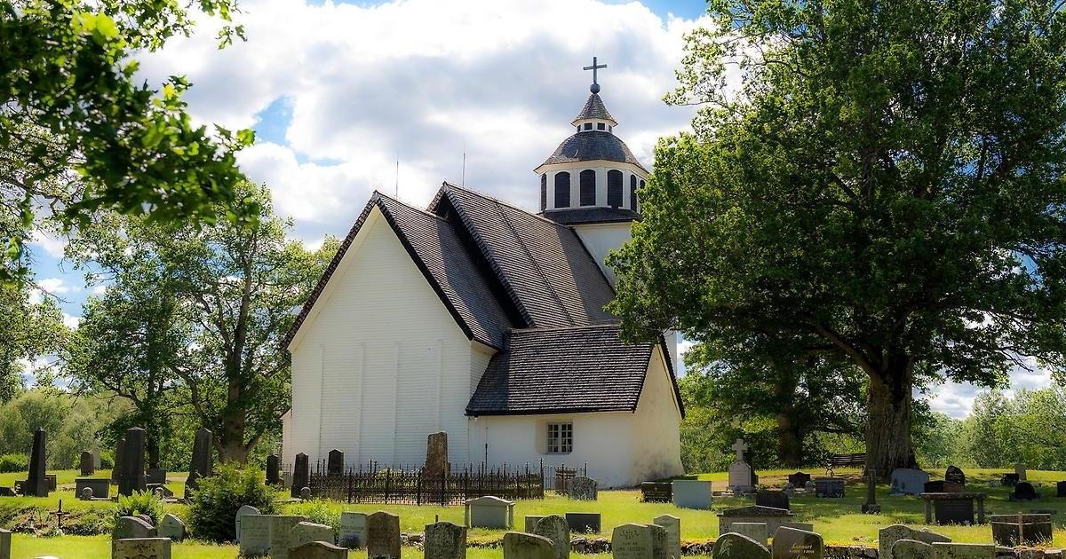 Stenberga kyrka mitt på kyrkogården, omges av träd och grönska.