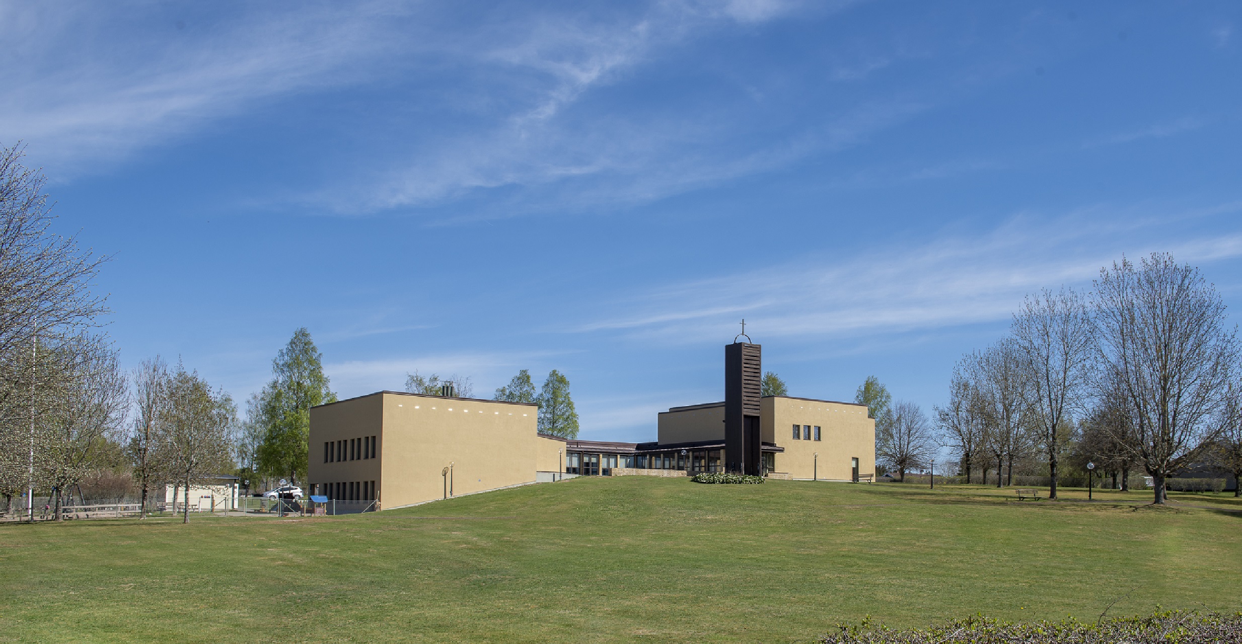 Ekenässjöns kyrka sedd från väster, spirande grönska och blå himmel.