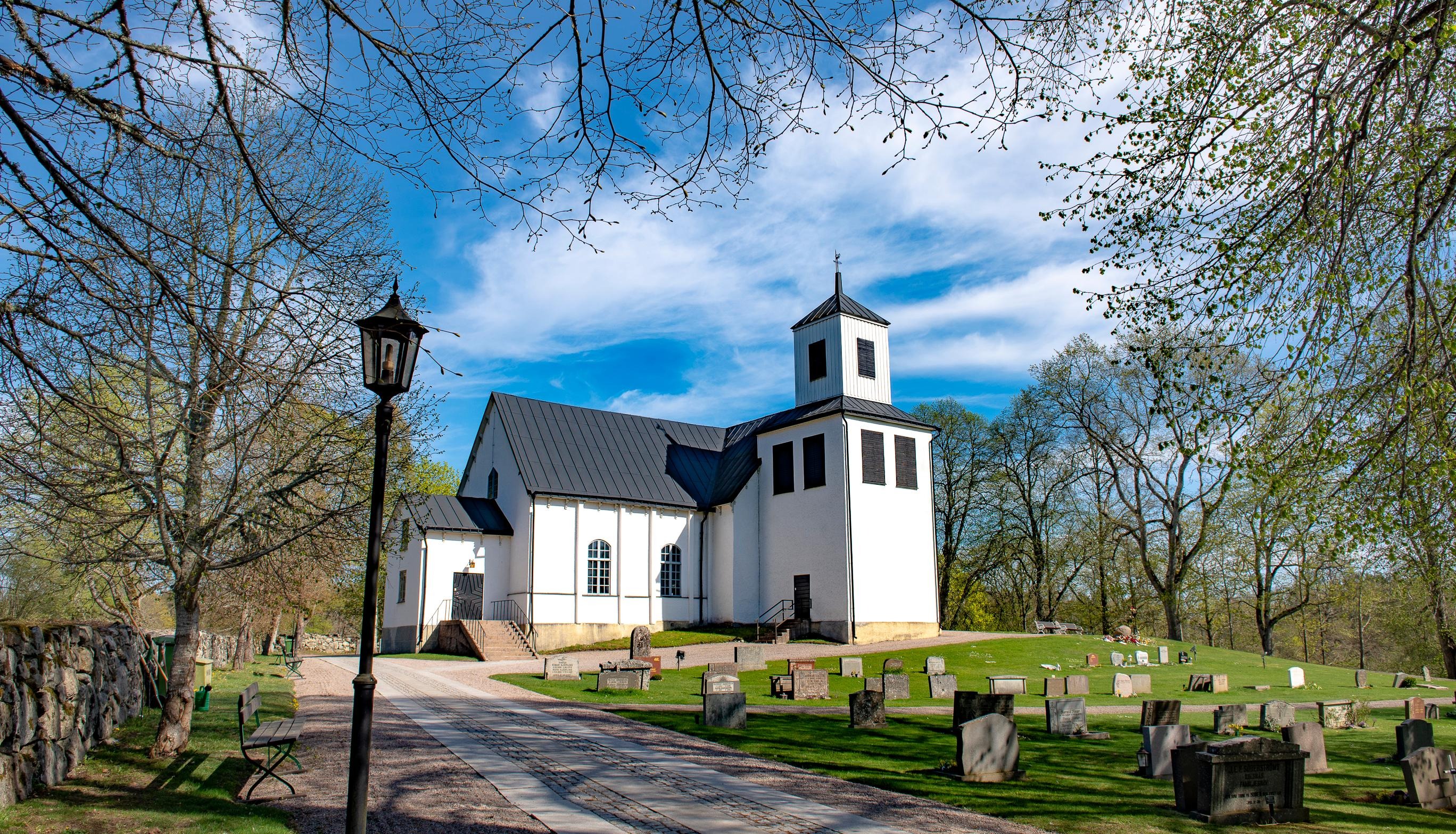 Näsby kyrka omgiven av kyrkogården och träd med knoppande grönska.