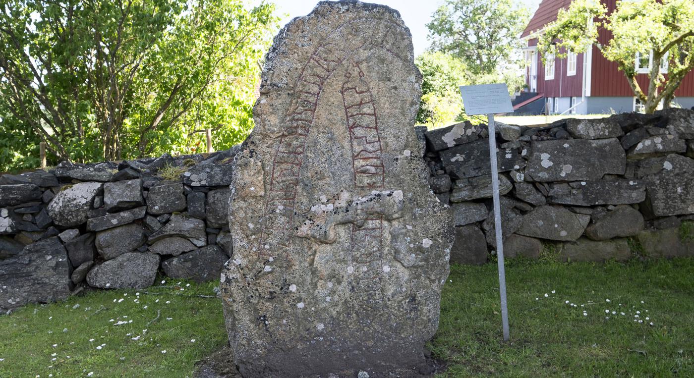En stor runsten framför en stenmur.