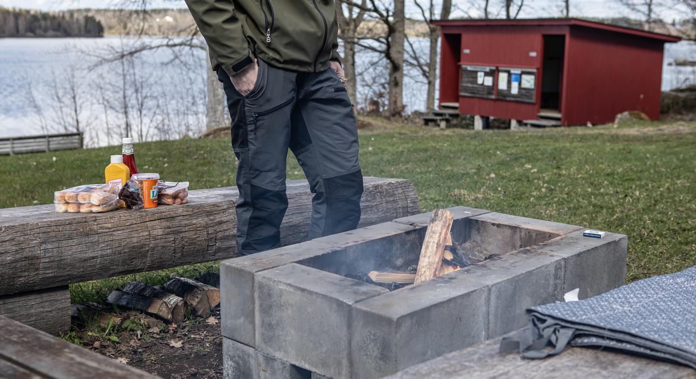 En person står vid en murad grillplats vid en sjö.