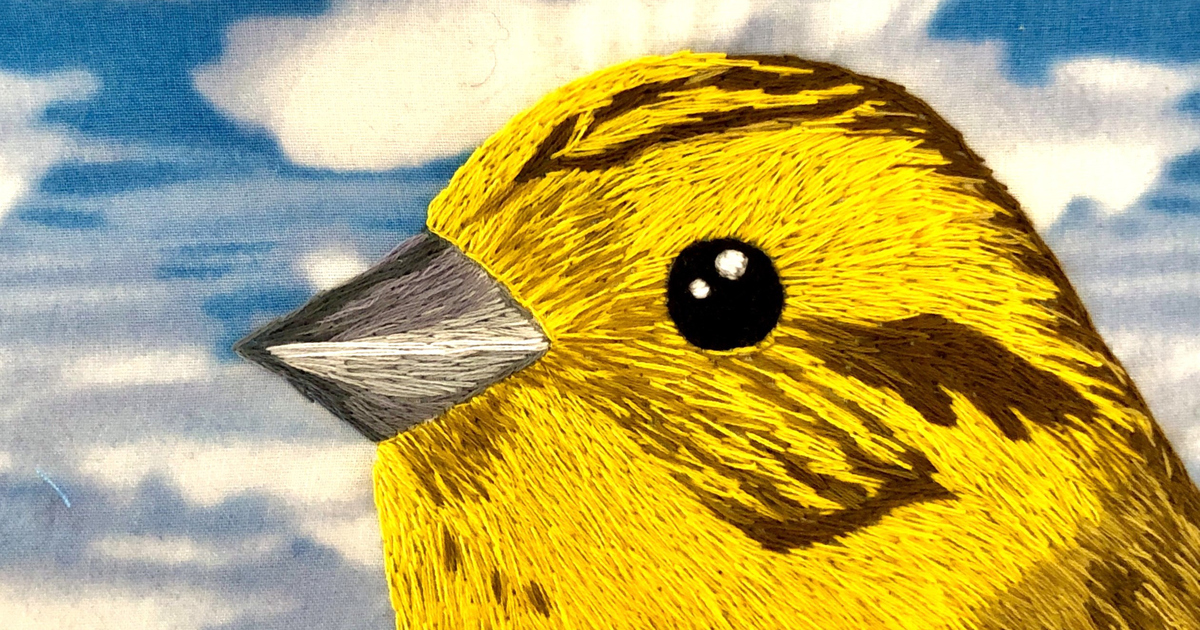 En broderad tavla föreställande en gul fågel