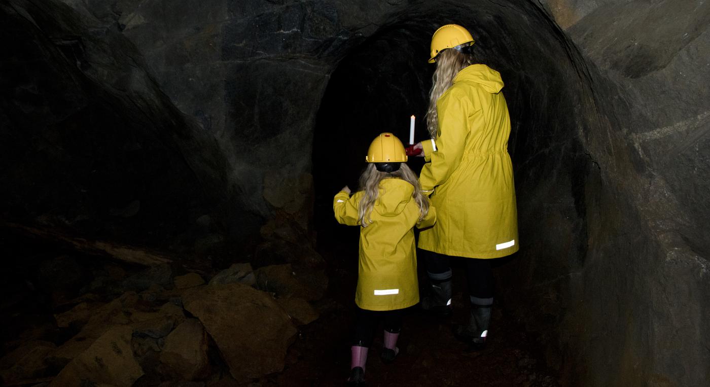 En mamma och dotter går med gula regnrockar och gula skyddshjälmar genom en gruva.