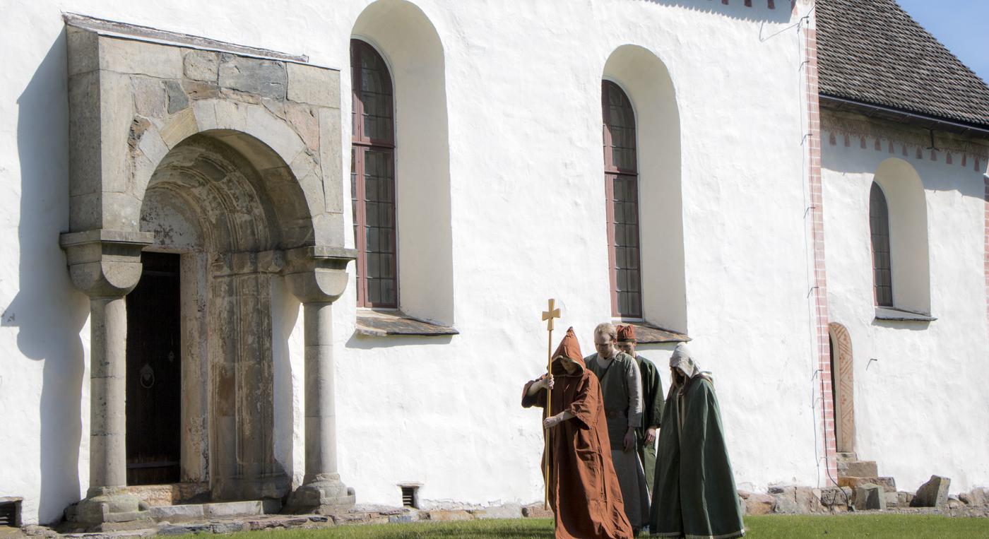 Personer i medeltidskläder är på väg in i en kyrka.