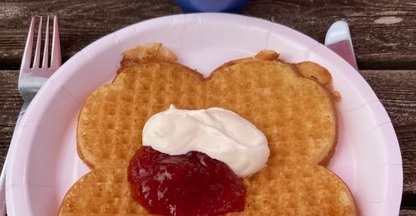En våffla med sylt och grädde, samt en blå kopp.