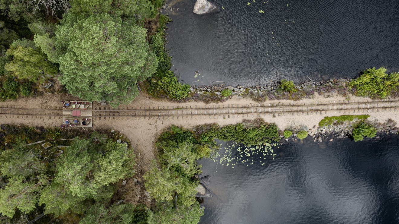 Ett järnvägsspår sett ovanifrån, på en vall omgiven av vatten.