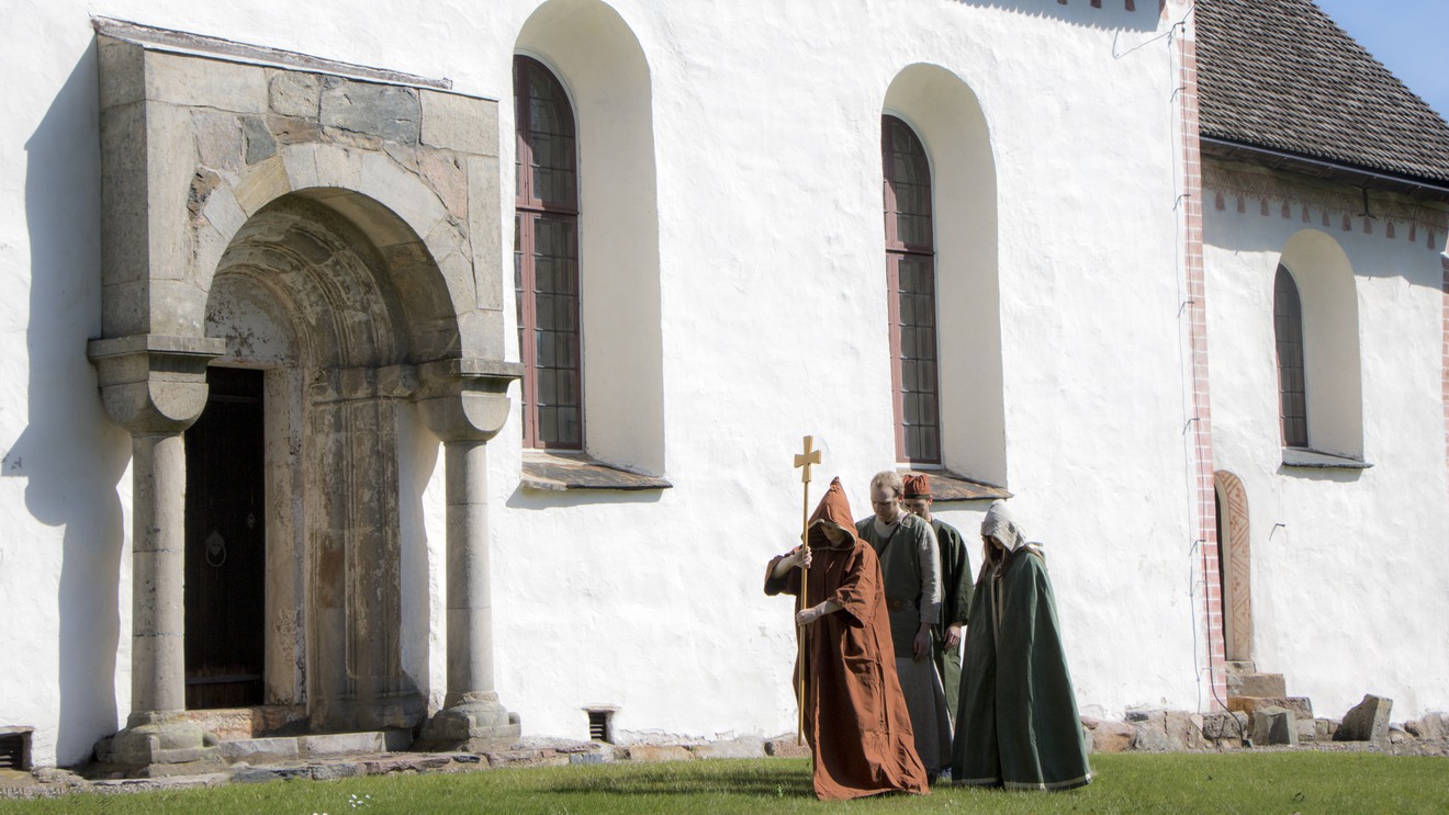 Fyra personer med medeltidskläder går mot Lannaskede gamla kyrkas ingång.