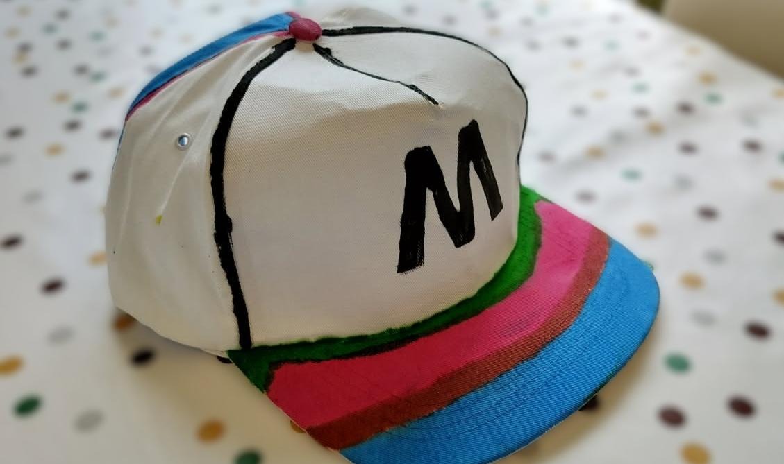 Bilden visar en keps som är målad i olika färger med ett M skrivet på framsidan.