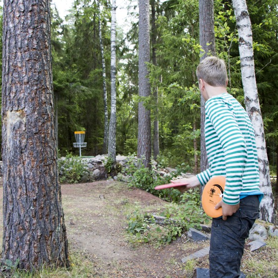 Pojke spelar discgolf i skogsmiljö.