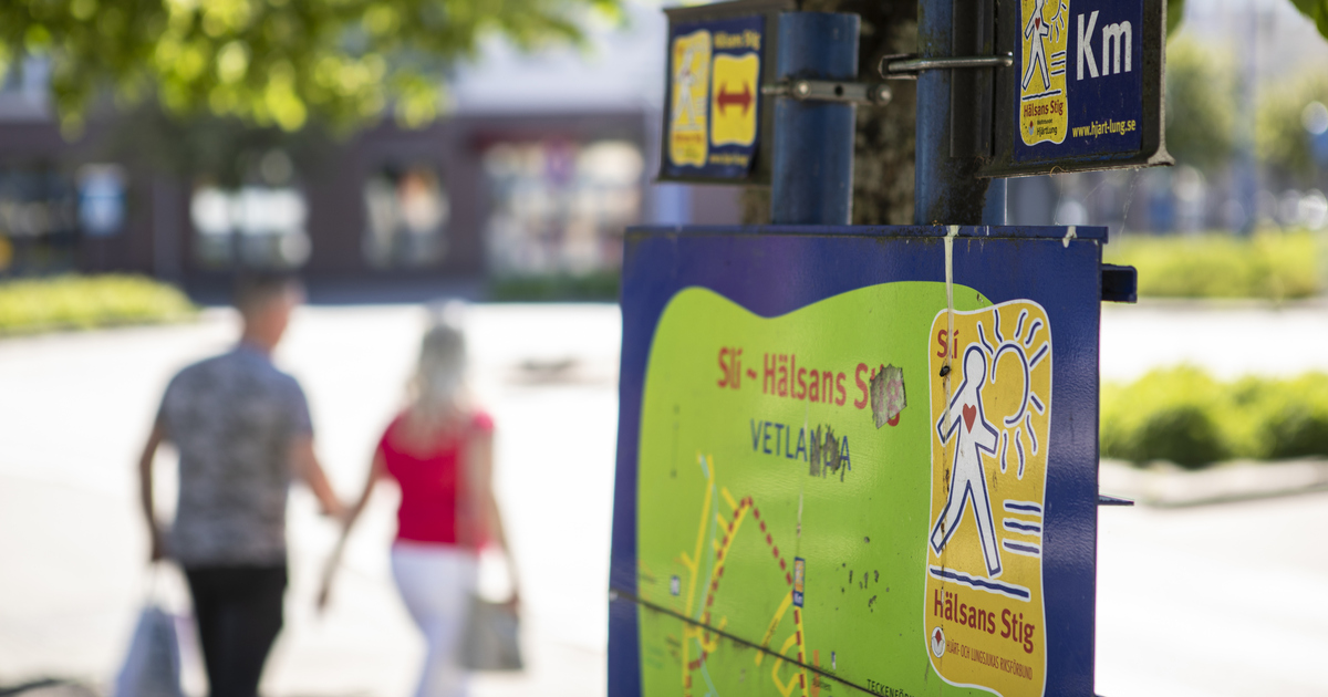 Skylt med Hälsans stig och personer som promenerar genom Vetlanda.