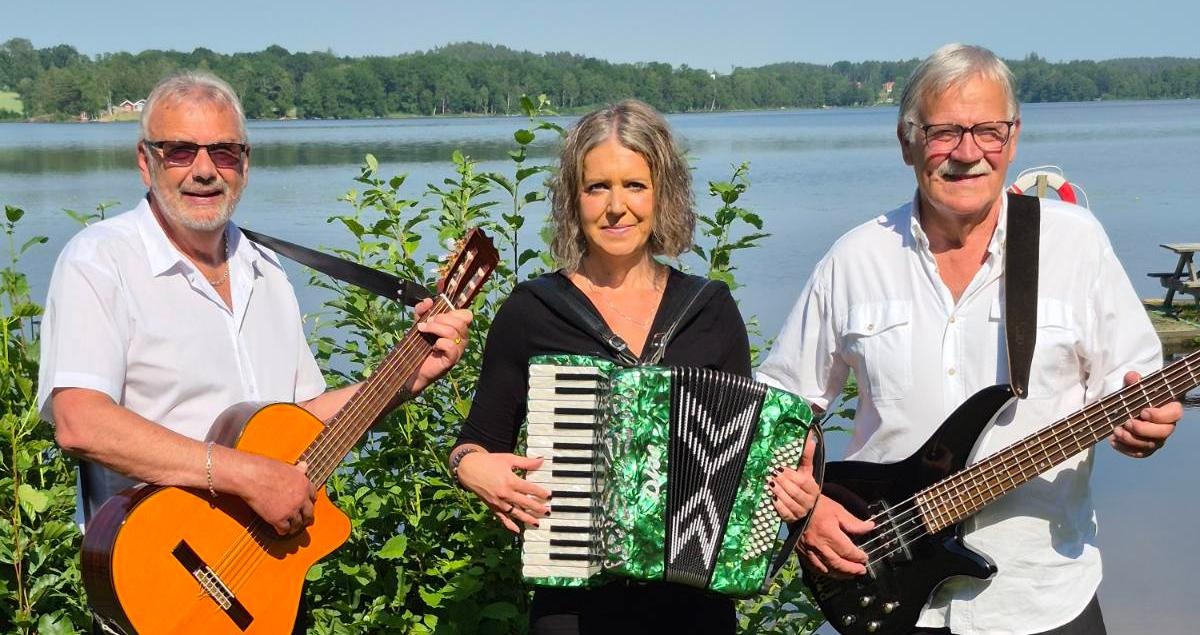 Två män med svarta byxor och vit skjorta med varsin gitarr och bas. Mellan dem står en kvinna i svart klänning med ett dragspel.