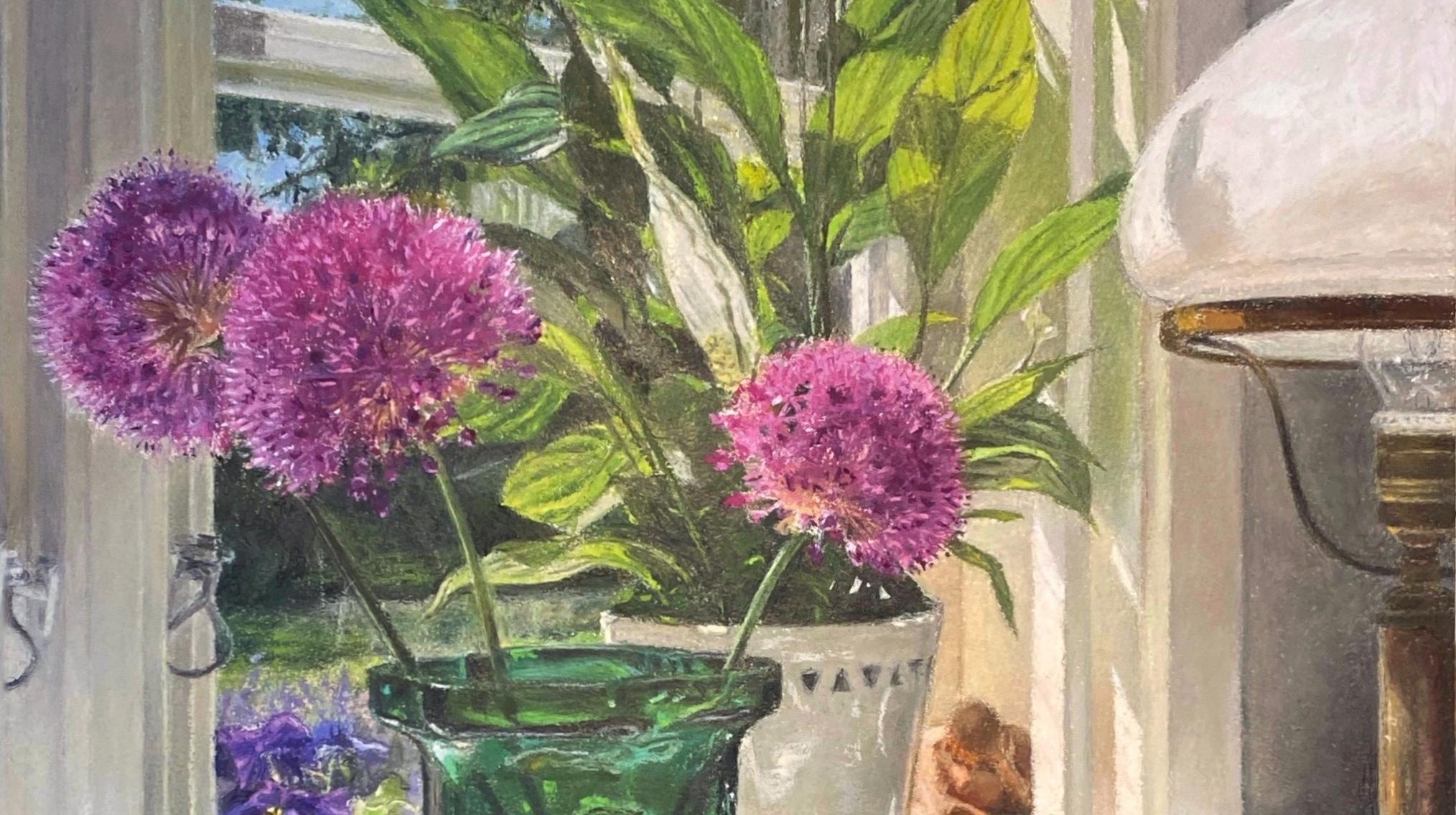 Bilden visar en grön glasvas med lila blommor och en apelsin bredvid vasen. I bakgrunden syns ett fönster med blomkrukor.