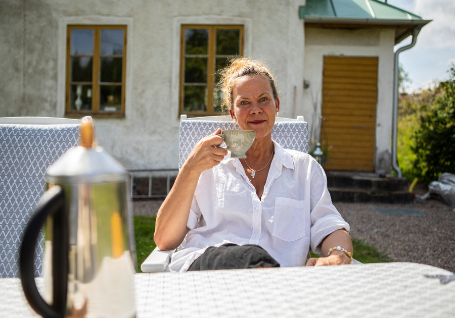 En kvinna sitter vid ett bord utomhus och håller upp en kaffekopp.