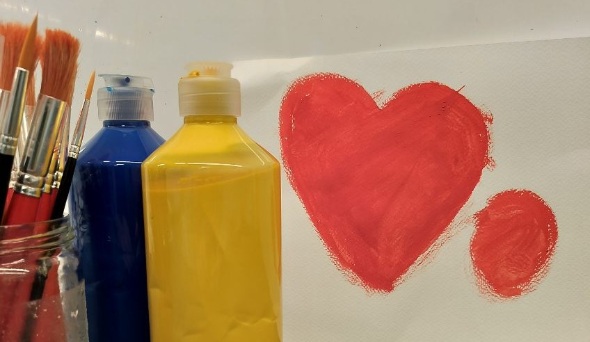 På bilden syns penslar, färgburkar och en målning föreställande ett hjärta