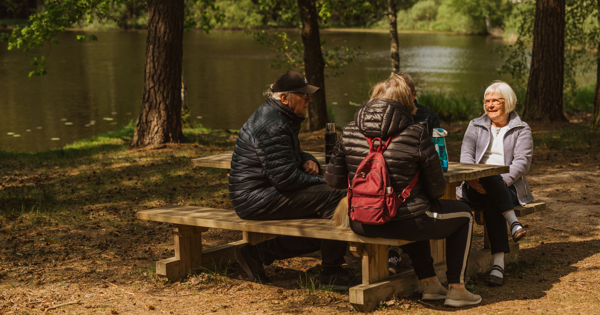 Personer som sitter och fikar runt ett bord i skogen