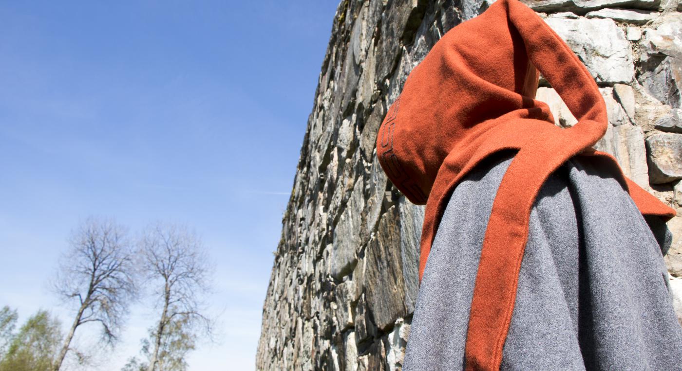 En person med medeltidskläder rör sig längs Hultaby slottsruins stenväggar.