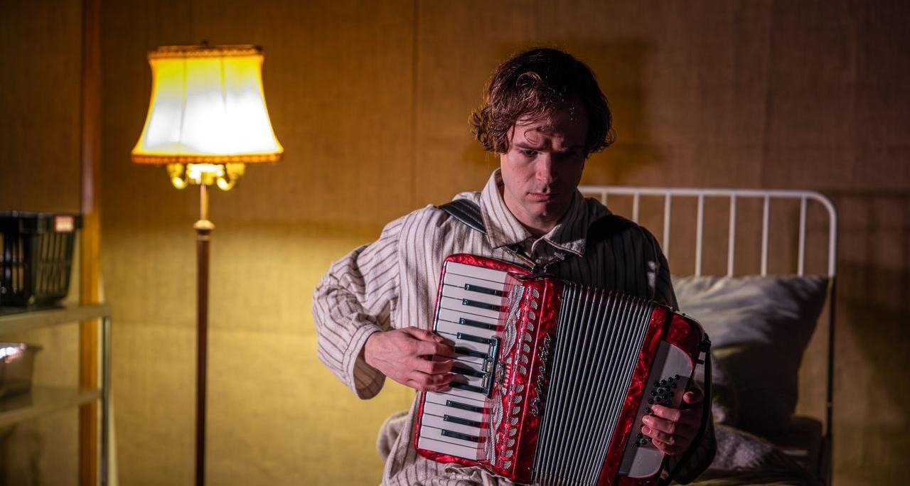 Erik Nilsson sitter på en sjukhussäng och spelar dragspel