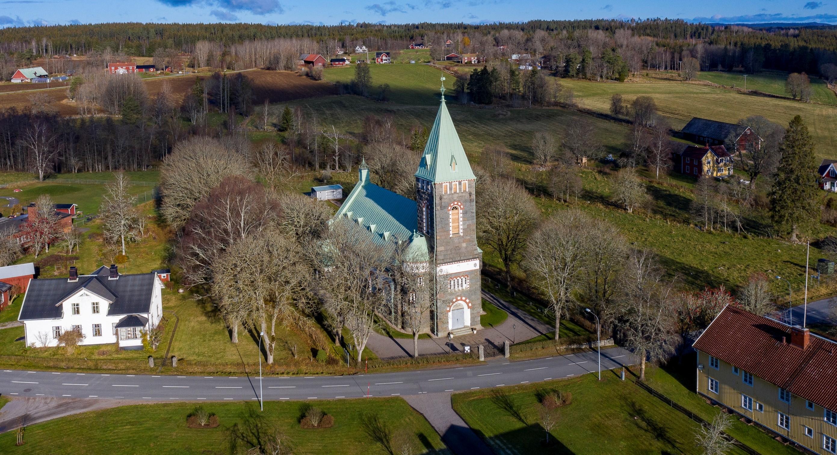 Flygbild på Bäckaby kyrka, gröna gräsmattor men inga löv på träden.