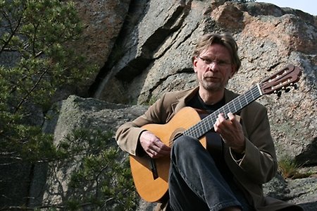 Eric Lammers står med en gitarr framför en berghäll.